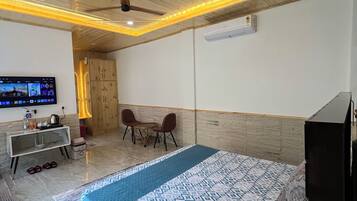 Habitación de hotel con cama, televisión, escritorio con silla, ventilador de techo y aire acondicionado.