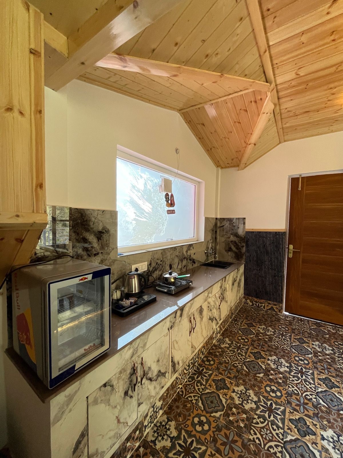 A kitchen with a marble countertop, a built-in microwave, and a window with a view of trees.