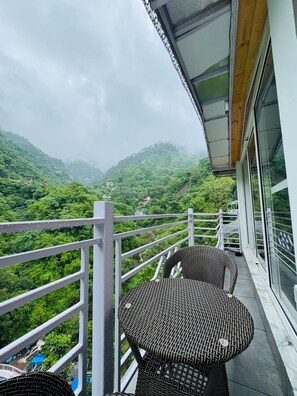 Un balcón con mobiliario de mimbre, barandilla blanca y vistas a un paisaje montañoso.