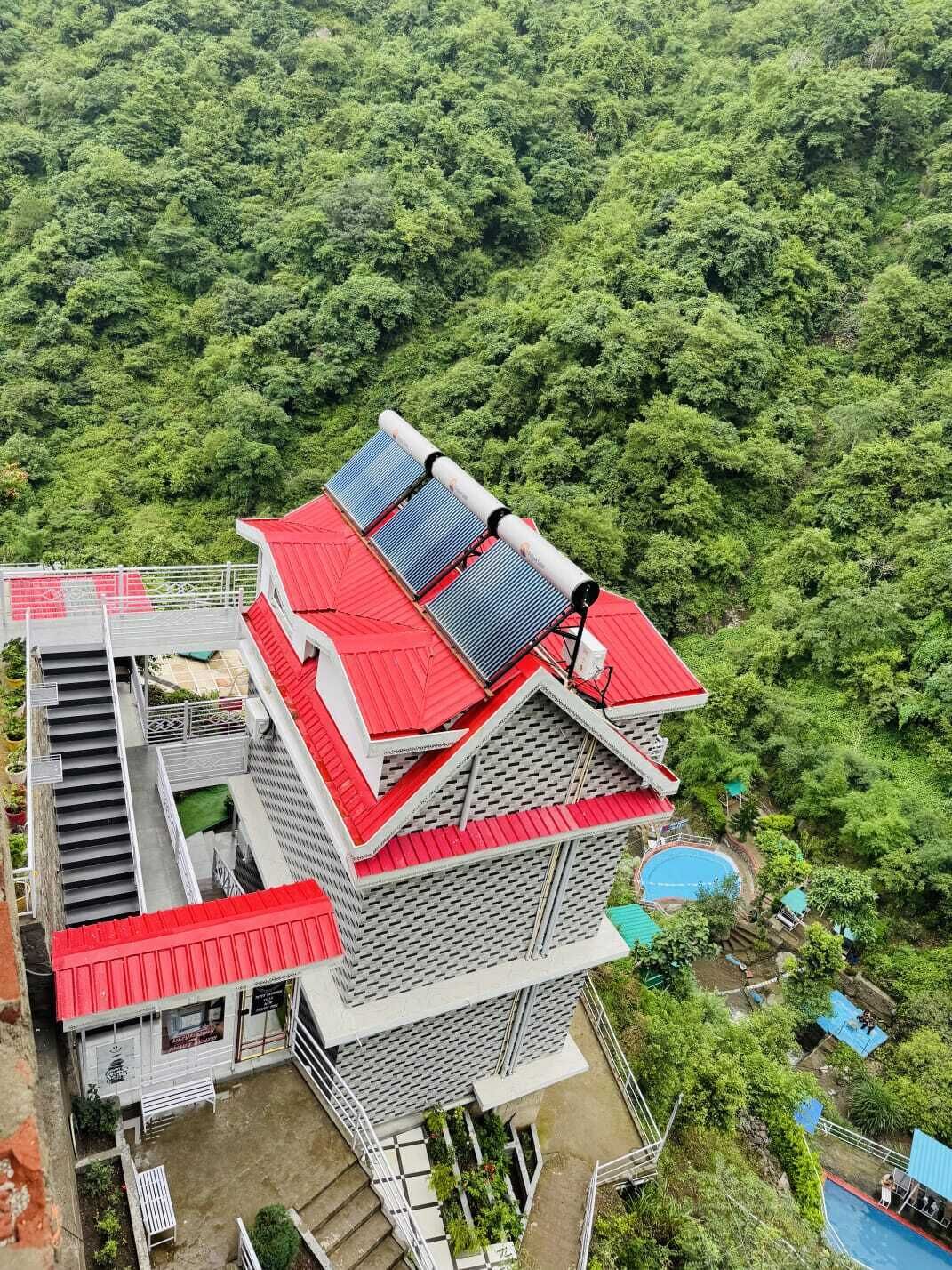 A multi-story building with a red roof, solar panels, and a swimming pool.