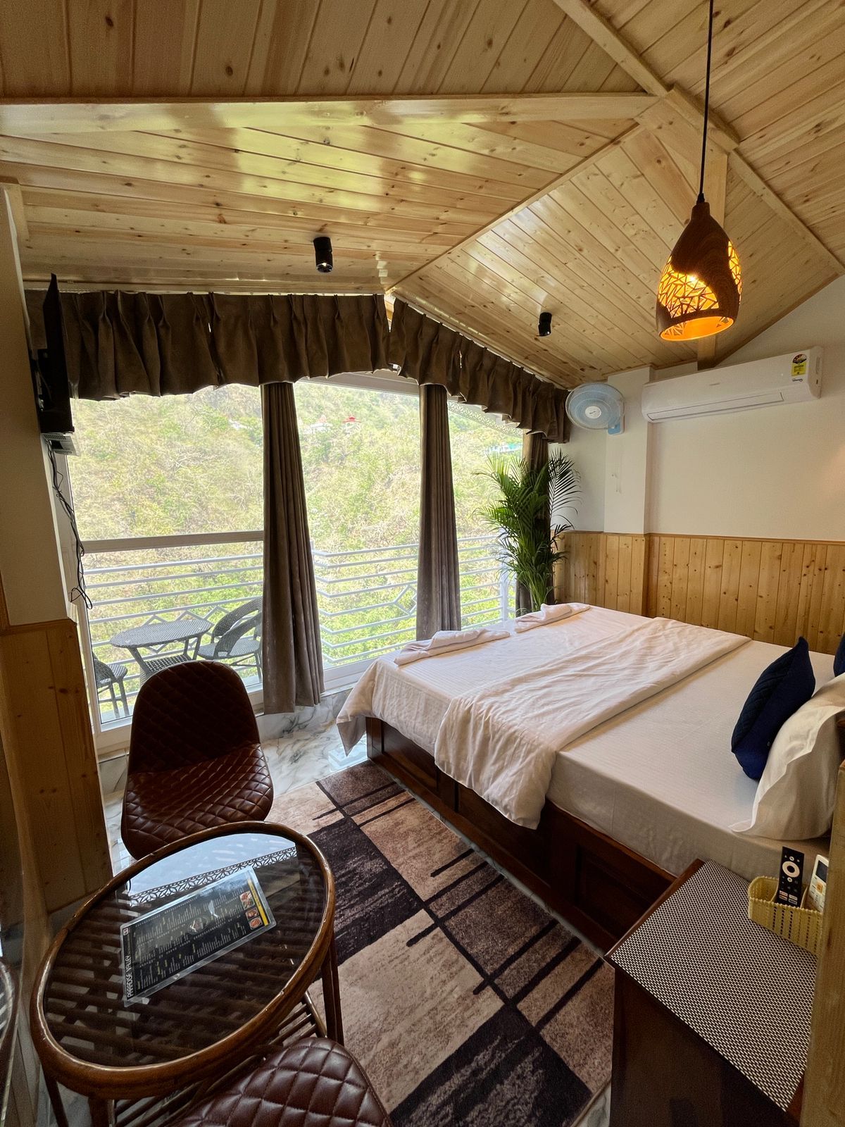 Habitación con paneles de madera, una cama, una mesa, una silla y vistas al exterior.