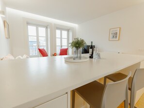 Ett modernt kök med vita bänkskivor, ett matbord och ett stort fönster.