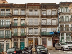 A row of multi-story buildings with balconies, a shop on the ground floor, and parked cars. - Apartment  by Interhome (Porto)