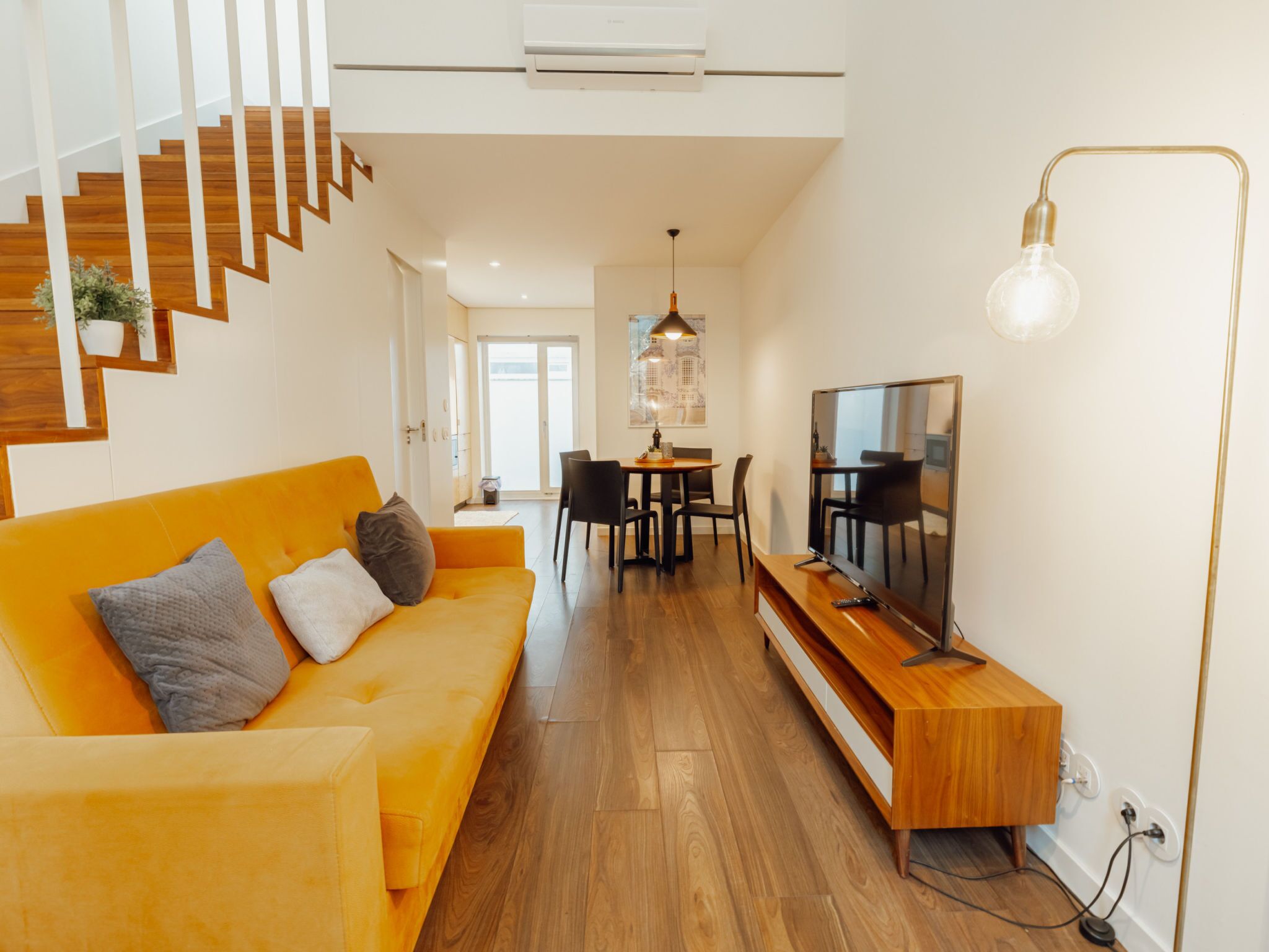 Un salon moderne avec un escalier en bois, un canapé, un coin repas et un téléviseur.