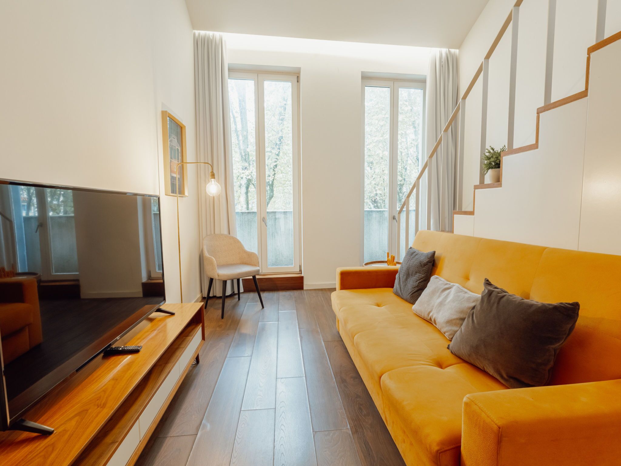 Ein modernes Wohnzimmer mit einer Couch, einem Fernseher, einem Sessel und einer Treppe.