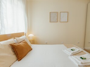 Quarto de hotel com cama, almofadas, mesa de cabeceira com abajur e duas obras de arte emolduradas na parede.