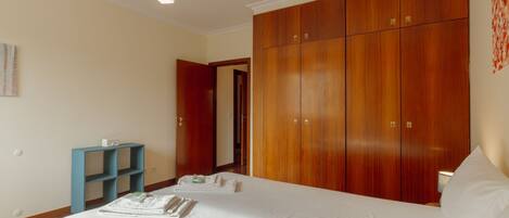A hotel room with a large bed, a wardrobe, a desk with a chair, and a hanging light fixture.