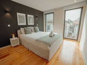 A modern bedroom with a large bed, bedside tables, and a view of the city through a large window. - Apartment  by Interhome (Porto)