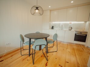 A modern kitchen with white cabinets, a round dining table with chairs, and a pendant light. - Apartment  by Interhome (Porto)