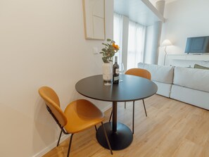Ein modernes Wohnzimmer mit einem runden Esstisch, zwei Stühlen, einem Sofa und einem Fernseher.