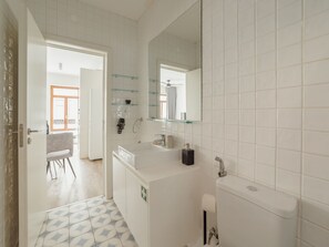 Ein modernes Badezimmer mit weißen Fliesen, einer Glasdusche, einer Toilette und einem Waschbecken mit Spiegel darüber.