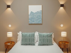 Ein Schlafzimmer mit einem Bett, zwei Nachttischlampen, einem gerahmten Kunstwerk über dem Bett und einer Wandleuchte.