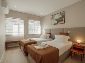 A hotel room with two beds, a bench, a bedside table with a lamp, and a painting on the wall. - Apartment  by Interhome (Porto)