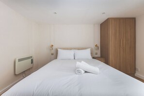 A hotel room with a large bed, a wooden wardrobe, and a radiator. - Stylish 2BDR 2BA Home with Patio in Putney (Greater London)