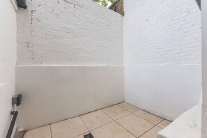 A small, enclosed outdoor space with white brick walls, a tiled floor, and a visible electrical outlet. - Stylish 2BDR 2BA Home with Patio in Putney (Greater London)