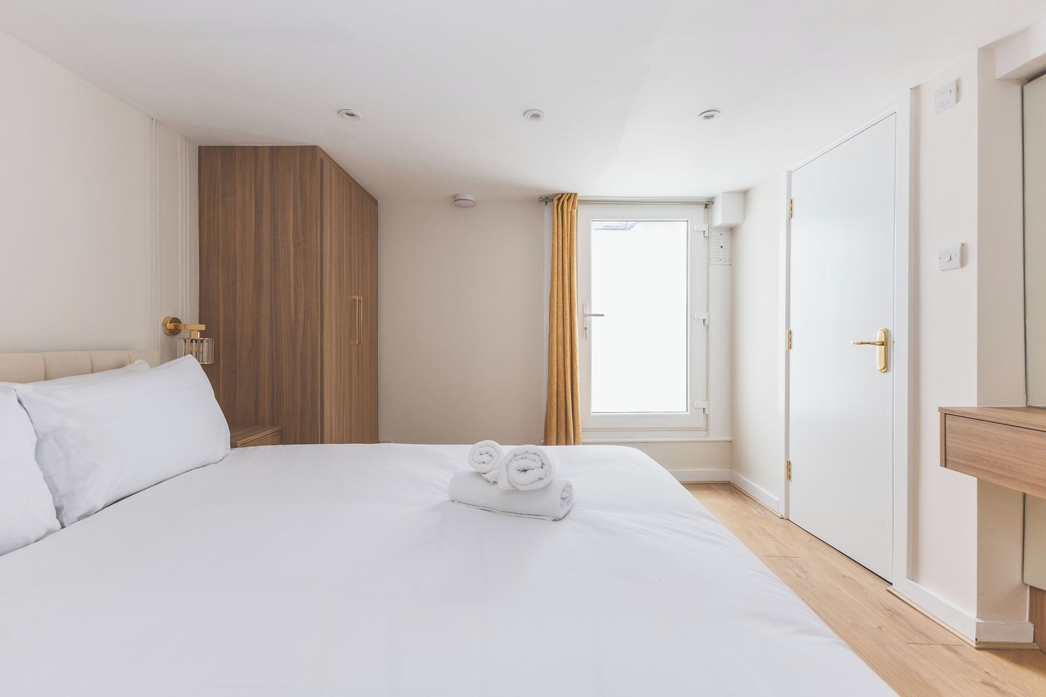 Une chambre d’hôtel avec un grand lit, une armoire en bois, une fenêtre avec des rideaux et une table de chevet en bois.