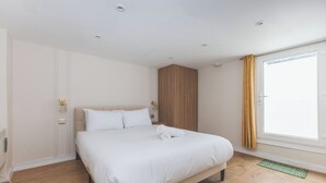 A hotel room with a large bed, wooden wardrobe, and a window with curtains. - Stylish 2BDR 2BA Home with Patio in Putney (Greater London)