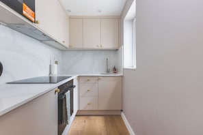 A compact kitchen with a built-in oven, a stovetop, and a window. - Stylish 2BDR 2BA Home with Patio in Putney (Greater London)