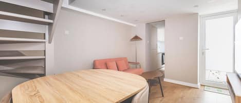 A modern interior with a wooden dining table, a sofa, and a staircase.