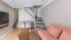 A modern living room with a flat-screen TV, a round wooden table, a pink sofa, and a staircase. - Stylish 2BDR 2BA Home with Patio in Putney (Greater London)