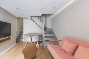 Ein modernes Wohnzimmer mit Flachbildfernseher, rundem Holztisch, rosa Sofa und einer Treppe.