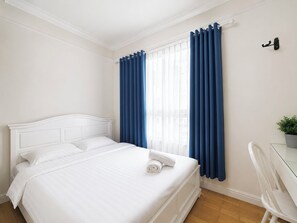 Ein Hotelzimmer mit einem weißen Bett, einem Glastisch, einem Stuhl und blauen Vorhängen.