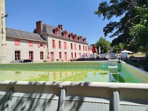 Une piscine offrant une vue sur une rangée d’immeubles aux volets rouges, avec un ciel bleu dégagé.