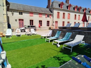 A courtyard with artificial grass, outdoor seating, and a parked car. - 18th century Castle of Clairefontaine (Garchizy)
