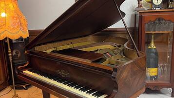 A grand piano in a room with a painting on the wall, a lamp, and a clock on a side table.