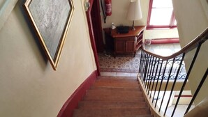 A wooden staircase with a handrail, leading to a landing with a fire extinguisher and a framed picture on the wall.