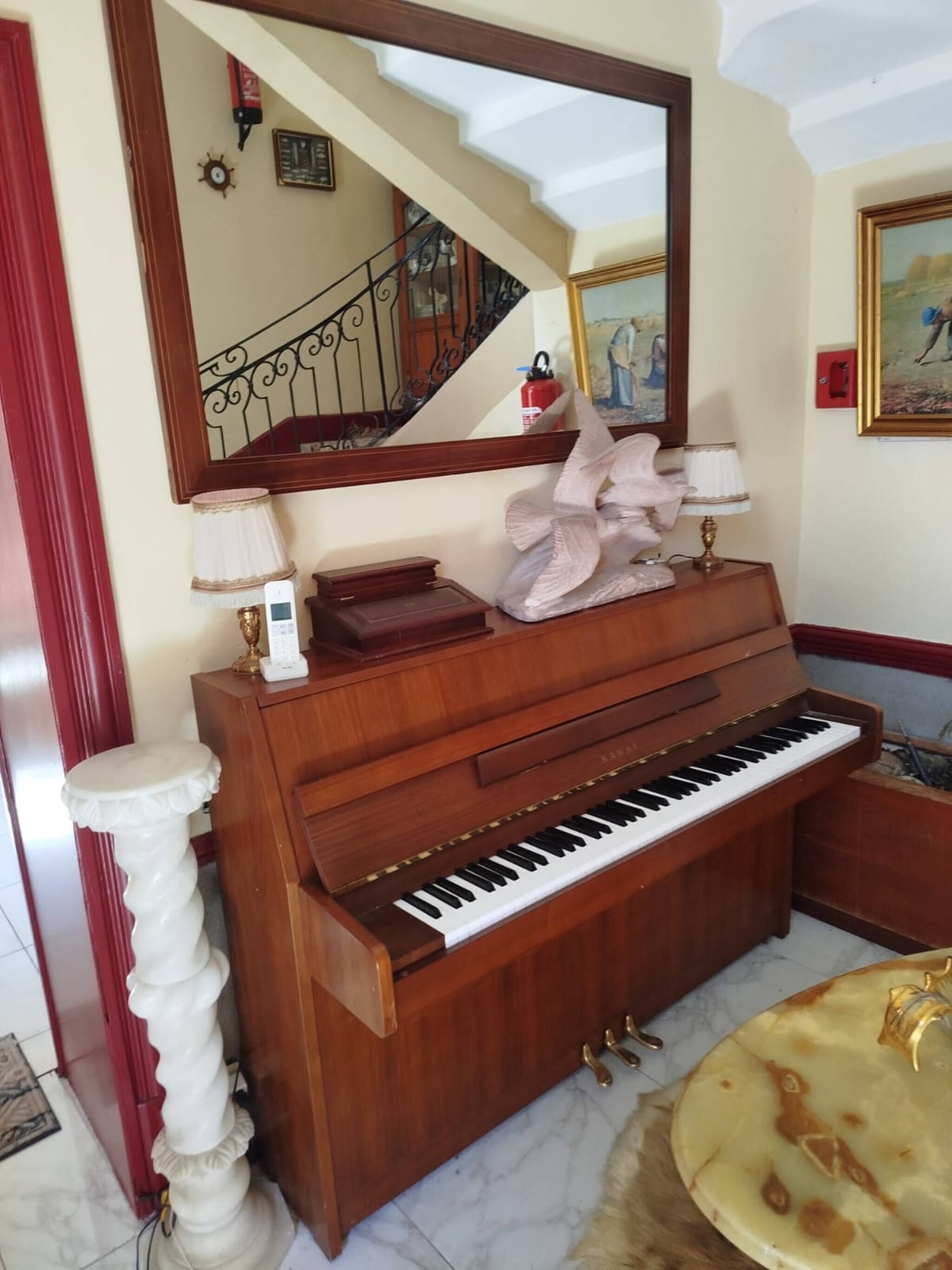 Un piano à queue dans une pièce au sol de marbre, avec un grand miroir au-dessus et un escalier en arrière-plan.