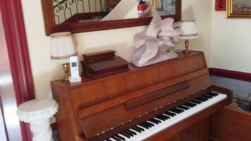 Un piano à queue dans une pièce au sol de marbre, avec un grand miroir au-dessus et un escalier en arrière-plan.