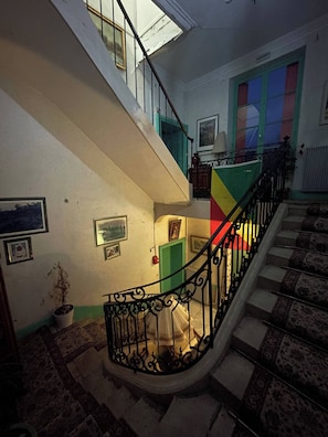 A staircase with ornate black railings, a potted plant, and a patterned carpet.