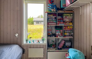 Ein Zimmer mit Fenster, Holzwänden, einem Bett und einem Regal mit verschiedenen Gesellschaftsspielen.