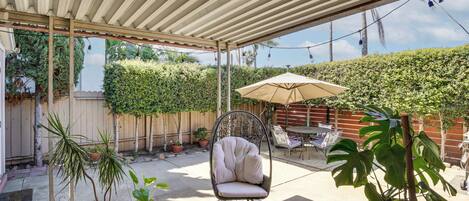 An outdoor patio area with a covered seating area, a table with chairs, and potted plants.
