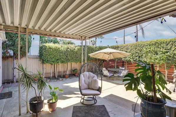 An outdoor patio area with a covered seating area, a table with chairs, and potted plants.