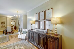 Ein gut beleuchtetes Wohnzimmer mit einem dunklen Holz-Konsolentisch, einem gestreiften Sessel und einem Essbereich mit einem Holztisch und Stühlen.