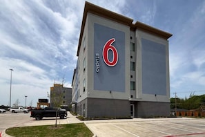Een modern gebouw met een opvallend bord met het cijfer '6', waarschijnlijk een hotel of appartementencomplex, met een parkeerplaats ervoor.