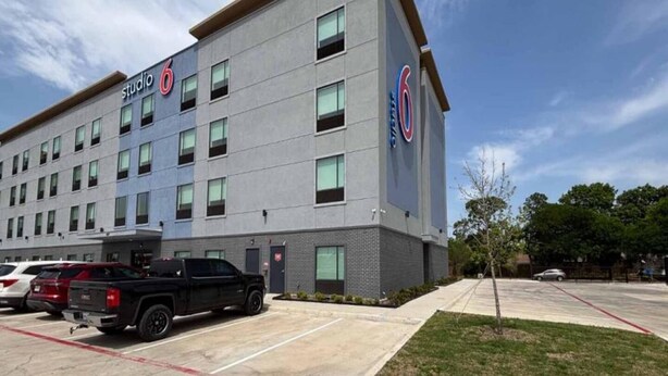 A multi-story hotel with a modern design, labeled 'Studio 6,' featuring a parking lot with several vehicles. - 2 Queen Beds|Non-Smoking,Kitchen (Dallas)