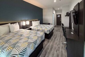 A hotel room with two beds, a desk, a wardrobe, and a television.