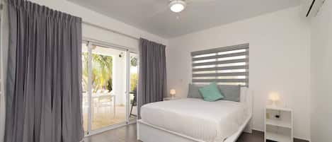 A bedroom with a bed, a ceiling fan, a window with blinds, and a sliding glass door leading to an outdoor area.