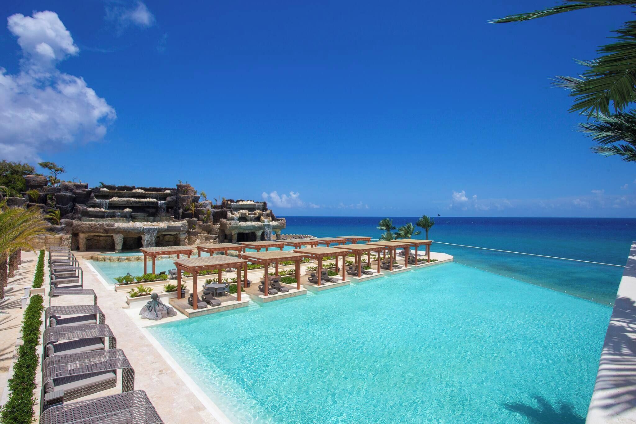 A resort with a clear blue pool, lounge chairs, and a view of the ocean.