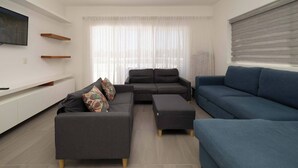 A modern living room with a grey sectional sofa, a blue sofa, and a TV mounted on the wall. - Villa Oasis del Mar 4 (Sosúa)
