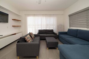 A modern living room with a grey sectional sofa, a blue sofa, and a TV mounted on the wall. - Villa Oasis del Mar 4 (Sosúa)