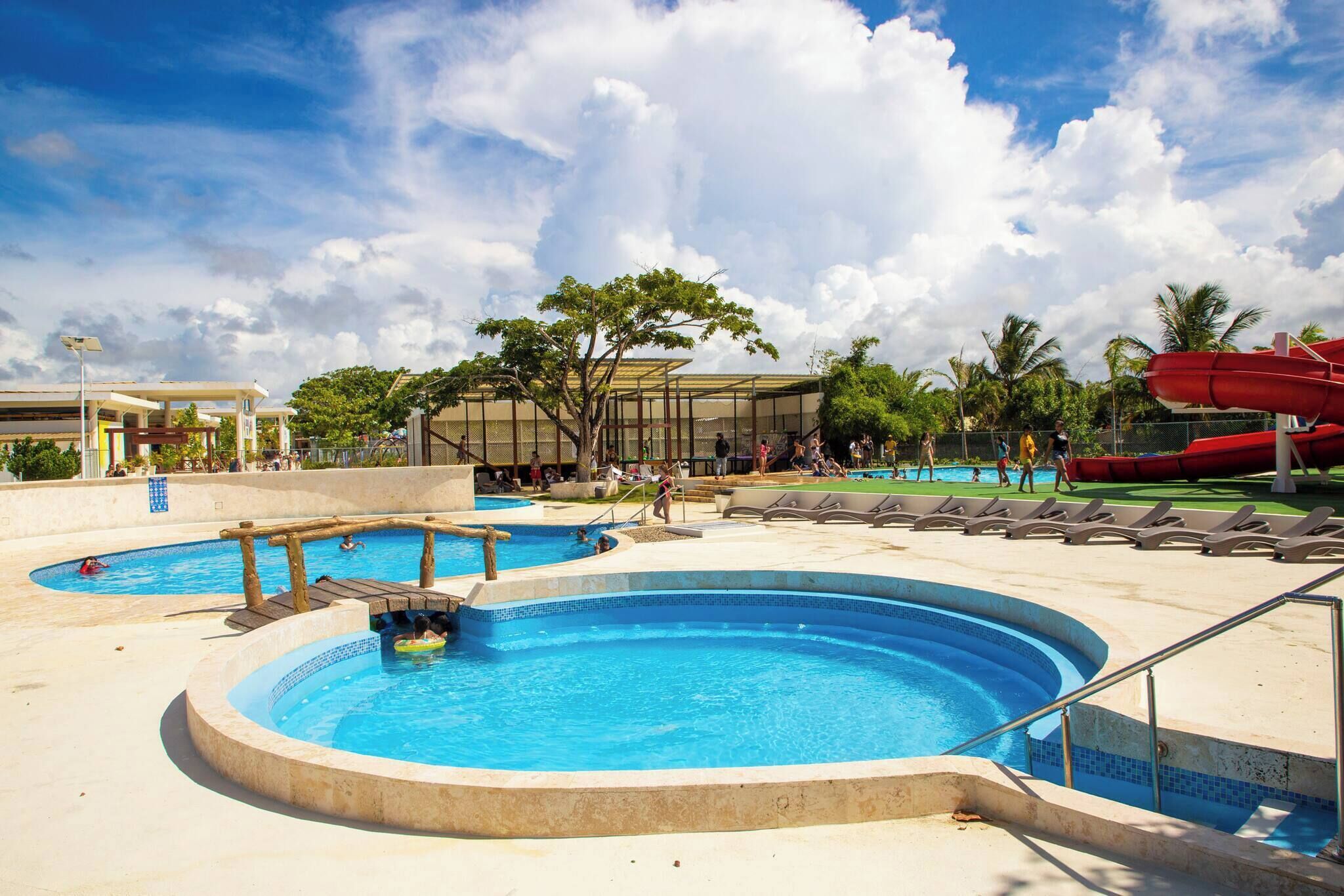 Un área de piscina con varias piscinas y un tobogán acuático rojo.