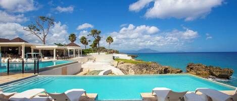A pool area with lounge chairs, a covered seating area, and a view of the ocean.