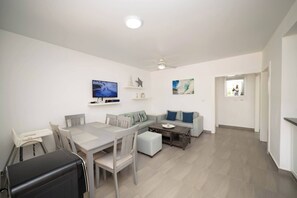 Uma sala de estar moderna com área de jantar, sofá, televisão de tela plana e ventilador de teto.