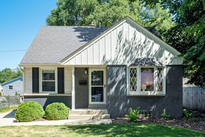 A single-story house with a gabled roof, a front porch, and a small front yard with a hedge and mulch. - Close to Downtown Milwaukee & Mid-Term Friendly! (Wauwatosa)