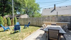 Een achtertuin met een patio tafel en stoelen, een houten omheining en een huis op de achtergrond.