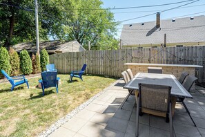 A backyard with a patio table and chairs, a wooden fence, and a house in the background. - Close to Downtown Milwaukee & Mid-Term Friendly! (Wauwatosa)